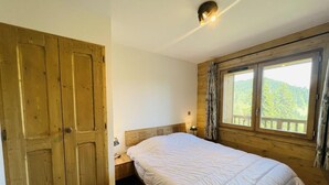 A bedroom with a large bed, wooden wardrobe, and a window with a view of greenery.