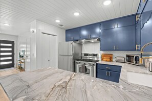 A modern kitchen with white cabinetry, a marble countertop, stainless steel appliances, and a built-in oven.