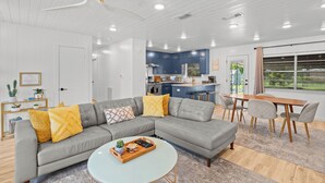 Een moderne woonkamer met een grijze modulaire bank, een ronde salontafel en een eethoek met een houten tafel en stoelen.