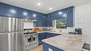 Een moderne keuken met roestvrijstalen apparatuur, blauwe kastjes en een marmeren aanrecht.