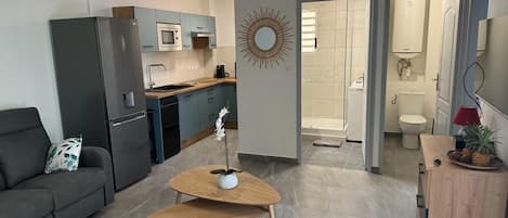 Un salon moderne comprenant un canapé, une table basse en bois et un coin cuisine équipé d’un réfrigérateur, d’un four à micro-ondes et de placards.