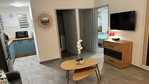 Sala de estar com uma mesa de jantar, televisão e cozinha ao fundo.