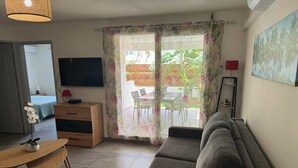 Uma sala de estar com sofá, mesa de madeira, televisão e porta de vidro deslizante que dá para um pátio com mobiliário de exterior.