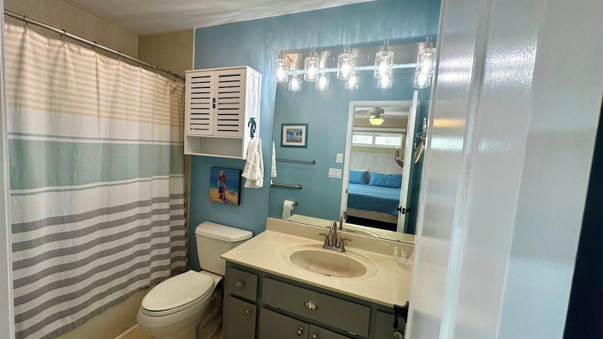 A bathroom with a striped shower curtain, a toilet, a sink with a mirror, and a towel rack.