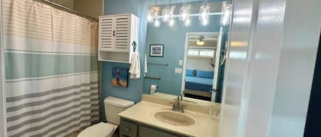 A bathroom with a striped shower curtain, a toilet, a sink with a mirror, and a towel rack.