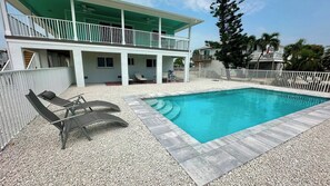 A two-story building with a swimming pool, outdoor seating, and a white fence.