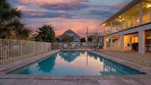 Ein rechteckiger Pool mit weißem Zaun an einer Seite, umgeben von einer Terrasse mit Blick auf Häuser im Hintergrund.