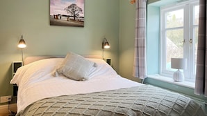 A bedroom with a bed, two bedside lamps, a window with curtains, and a painting on the wall.