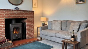 A cozy living room with a brick fireplace, a grey sofa, and a small wooden table with a bottle and glasses.