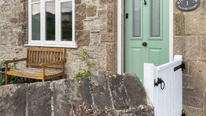 A stone cottage with a green door, a bench outside, and a sign reading "River View 1 Brookside Cottages".