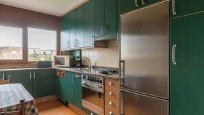 A compact kitchen with green cabinets, a stainless steel refrigerator, a microwave, and a stove. - Apartamento Playa del Sardinero (Santander)