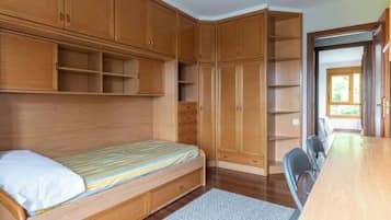 Een slaapkamer met een bed, een houten garderobe en een bureau met een stoel.