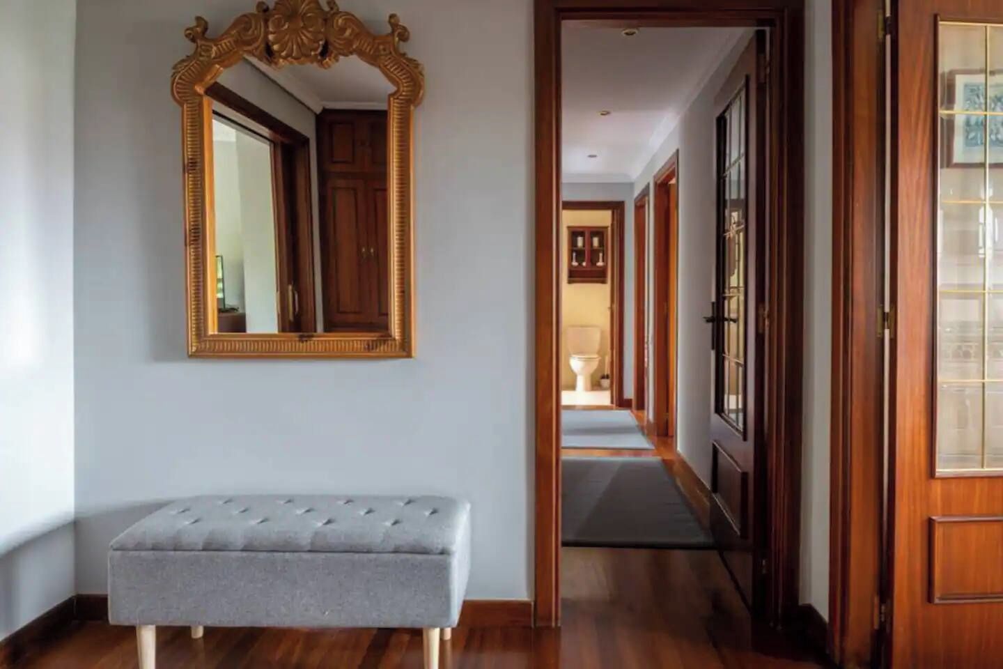 A hallway with a bench, a mirror, and a door leading to another room.