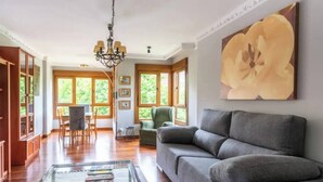 A living room with a sofa, a glass coffee table, a chandelier, and a painting. - Apartamento Playa del Sardinero (Santander)