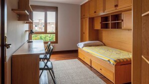 A compact bedroom with a single bed, a desk, and built-in wooden shelving. - Apartamento Playa del Sardinero (Santander)