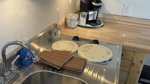 Lavello in acciaio inox con un solo rubinetto, una macchina da caffè e una pila di asciugamani marroni sul piano di lavoro.