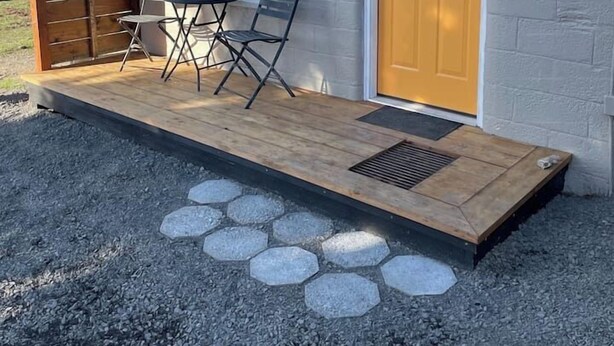 Un piccolo edificio con una terrazza in legno, un tavolo e due sedie.