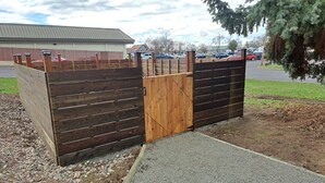 Un cancello in legno con maniglia metallica, che dà accesso a un vialetto sterrato e a una strada asfaltata.
