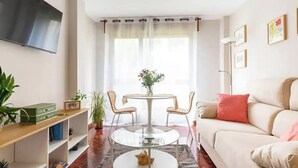 Una sala de estar con sofá, una mesa de centro, un televisor montado en la pared y un comedor con mesa y sillas.