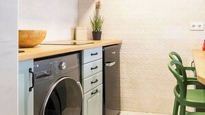 Eine kompakte Küche mit Waschmaschine, einem kleinen Schrank und einer Essecke mit einem Stuhl.