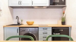 Cocina compacta con lavavajillas, microondas, pileta y un bol de madera en la encimera.