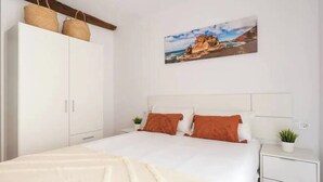 Una camera da letto con un letto, un'armadio bianco e un quadro raffigurante un paesaggio costiero.
