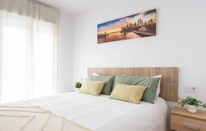 A bedroom with a bed, a headboard, a nightstand with a plant, and a wall-mounted painting.