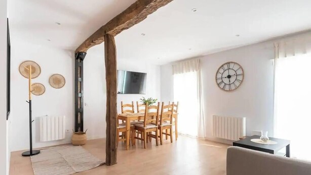 Un soggiorno spazioso con trave in legno a vista, una zona pranzo con mobili in legno, un orologio appeso al muro e un termosifone.