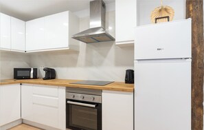 A modern kitchen with white cabinets, a stainless steel range hood, a built-in oven, and a white refrigerator.