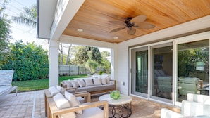Une terrasse extérieure avec des meubles en bois, un ventilateur de plafond et une porte vitrée donnant sur un jardin.