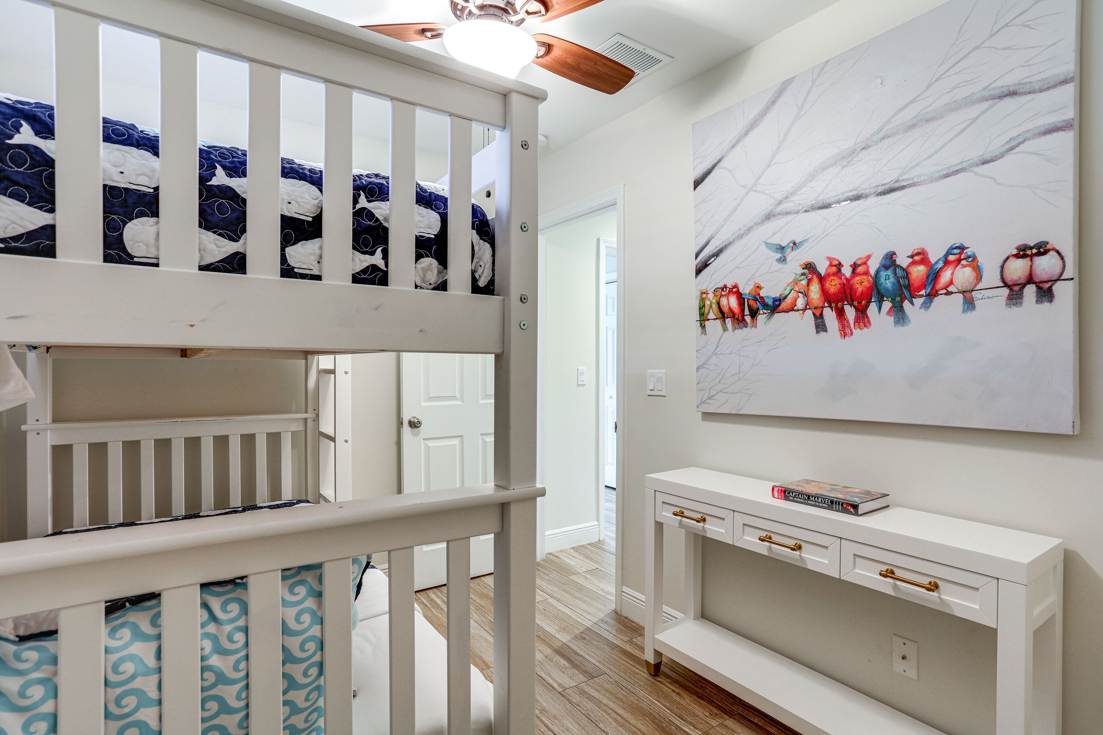 A room with a bunk bed, a white console table with drawers, and a wall-mounted painting of birds.