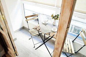 A modern dining area with a table set for two, a vase with flowers, and a view of the city through large windows.