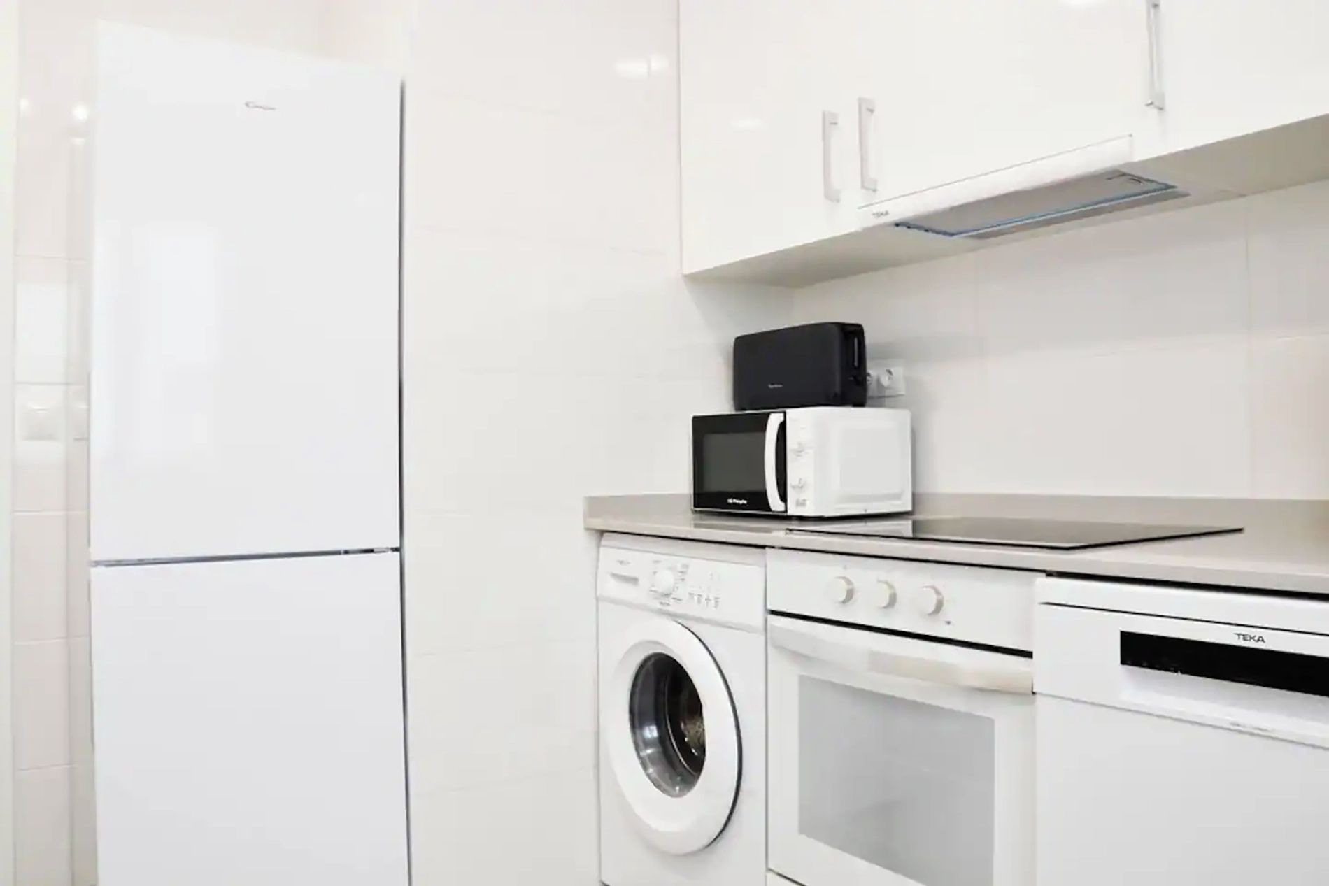 A kitchen with a refrigerator, microwave, oven, and washing machine.