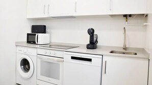 A compact kitchen with white cabinetry, a microwave, a coffee machine, a washing machine, and a sink. - Nuevo Apartamento con 3 dormitorios (Santander)
