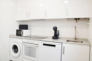 A compact kitchen with white cabinetry, a microwave, a coffee machine, a washing machine, and a sink. - Nuevo Apartamento con 3 dormitorios (Santander)