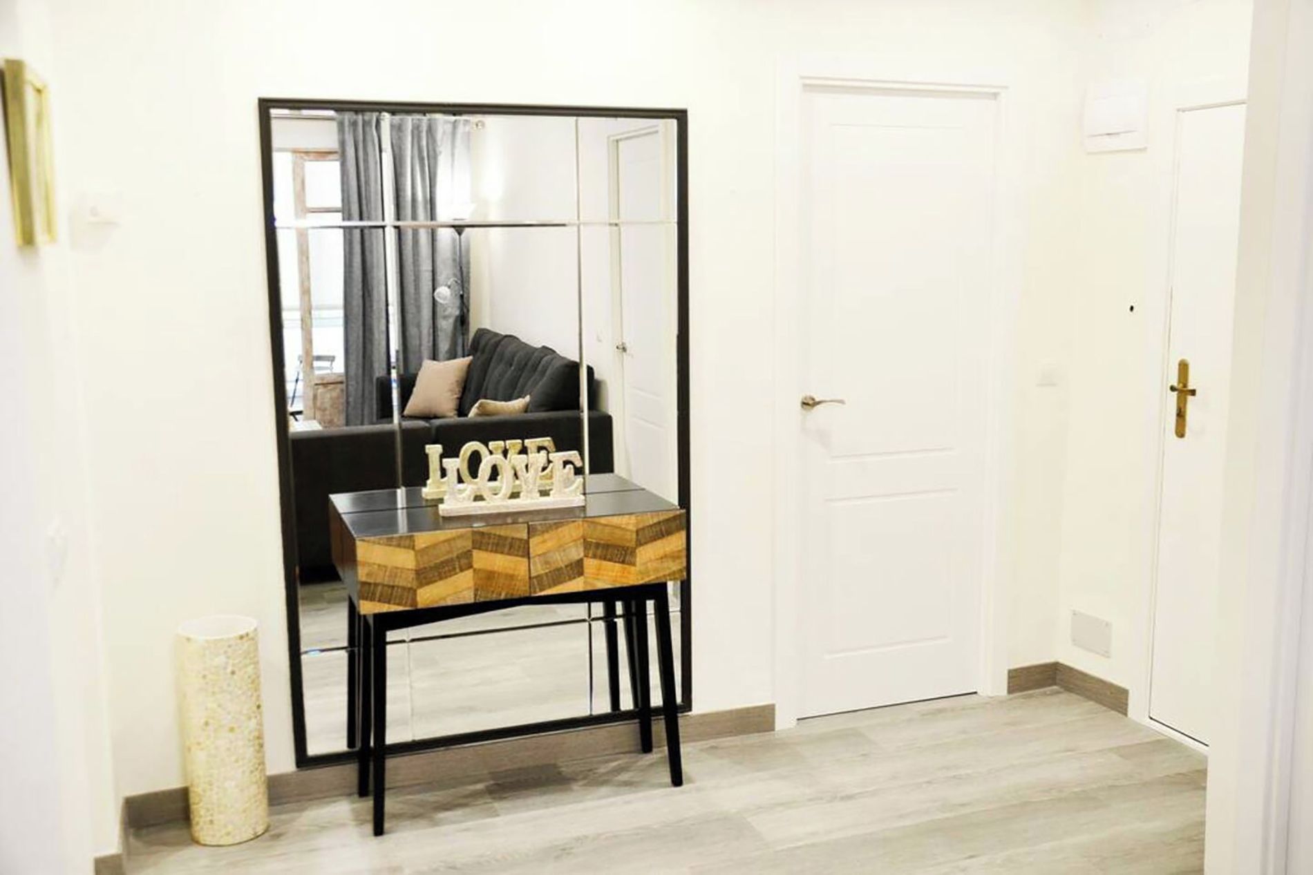 A room with a mirrored wardrobe, a small table with a 'LOVE' sign, and a door.
