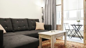 A modern living room with a dark grey sofa, a wooden coffee table, and a view of a balcony with a table and chairs. - Nuevo Apartamento con 3 dormitorios (Santander)