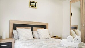 Een net opgemaakt bed met een beddeken met bloemenprint, een houten hoofdbord en twee nachtkastjes met lampen en een klein fotolijstje.