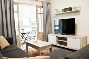 A living room with a sofa, a coffee table, a TV on a wooden stand, and a window with curtains. - Nuevo Apartamento con 3 dormitorios (Santander)