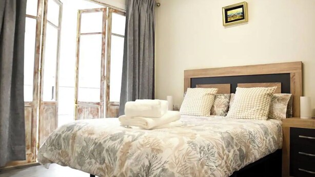 Een slaapkamer met een bed, een nachtkastje, een ingelijste foto aan de muur en een raam met gordijnen.