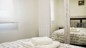 A bedroom with a bed covered in white linens, a bedside table, and a radiator. - Nuevo Apartamento con 3 dormitorios (Santander)
