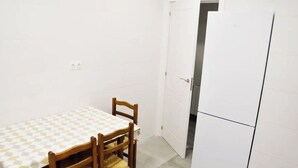 A small, clean room with a dining table and chairs, a white refrigerator, and a door leading to another room. - Nuevo Apartamento con 3 dormitorios (Santander)