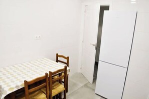 A small, clean room with a dining table and chairs, a white refrigerator, and a door leading to another room. - Nuevo Apartamento con 3 dormitorios (Santander)