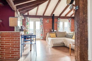 Een gezellige woonkamer met een bakstenen muur, houten balken, een bank en een eettafel met stoelen.