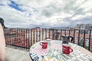 Een balkon met uitzicht op een stadsbeeld, twee Nescafé mokken en een koffiezetapparaat.