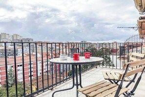 Een balkon met een ronde tafel, twee stoelen en twee rode mokken.