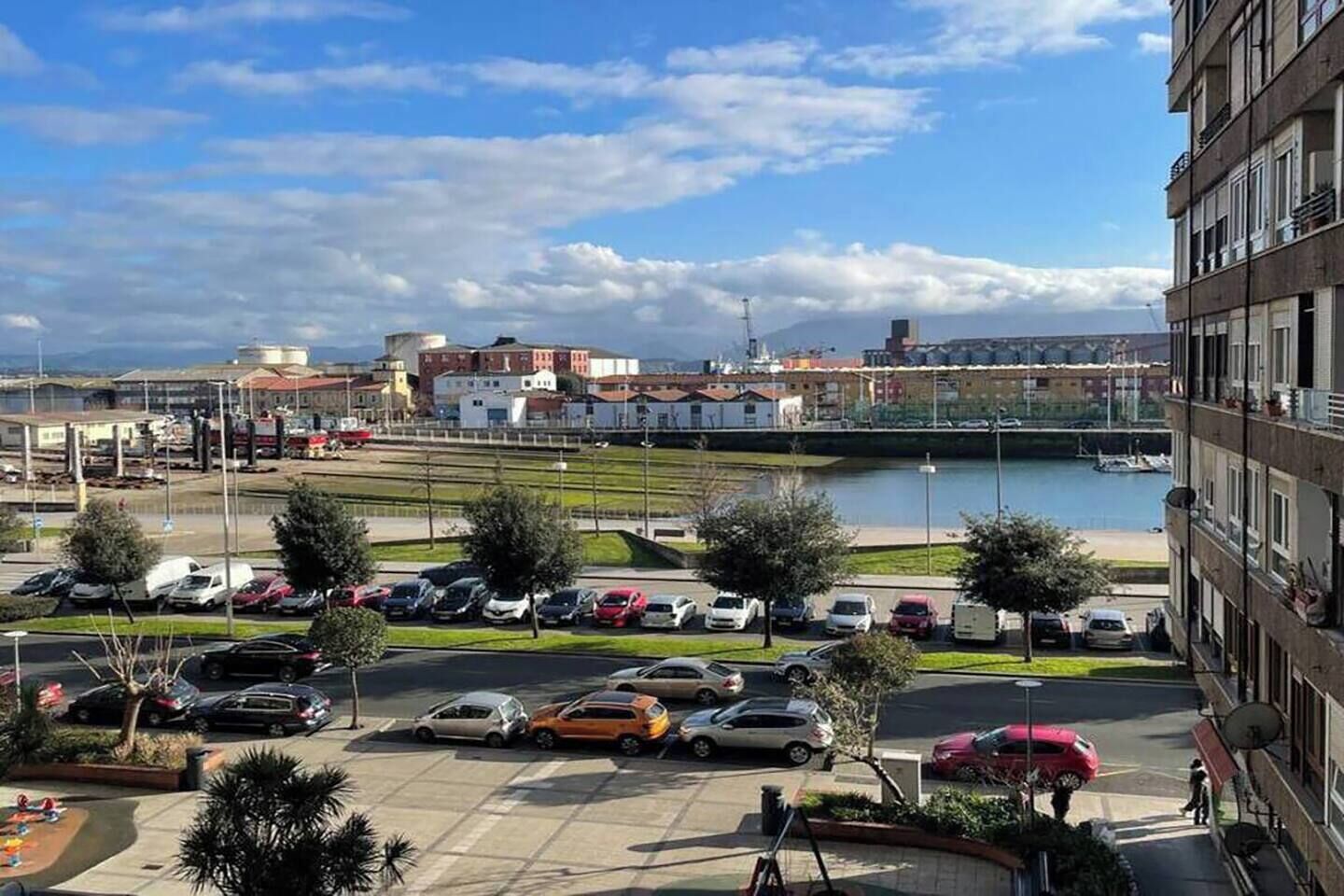 A parking lot with multiple cars, a body of water, and buildings in the background.