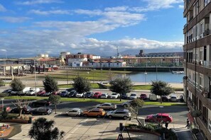 Un estacionamiento con varios autos, un cuerpo de agua y edificios al fondo.