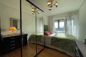 Un dormitorio con cama, cómoda, espejo y ventana con cortinas.