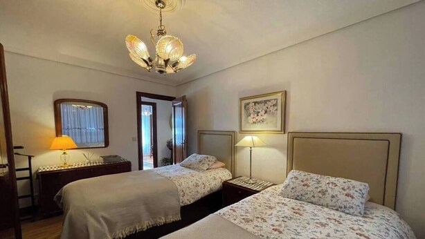 A hotel room with two beds, a chandelier, a desk with a lamp, and a door leading to a balcony. - Elegante apartamento con vistas al puerto (Santander)